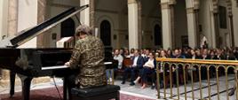 Pianista siedzi przy fortepianie i gra, w tle publiczność siedząca w ławkach kościoła 