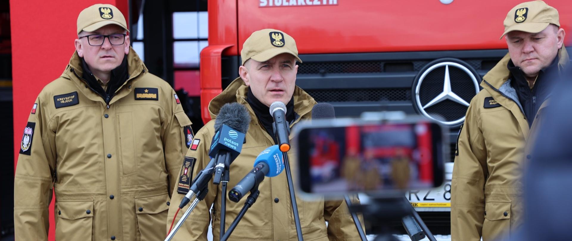 Stoją przy mikrofonie podczas konferencji prasowej - komendant główny PSP nadbryg. Andrzej Bartkowiak oraz jego zastępca nadbryg. Krzysztofa Hejduk i podkarpacki komendant wojewódzki PSP nadbryg. Andrzej Babiec.