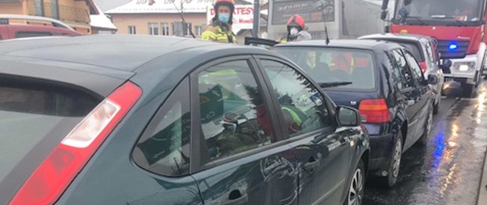 Na zdjęciu widoczne 3 samochody osobowe , które na siebie najechały. Za nimi w oddali widoczny samochód pożarniczy.