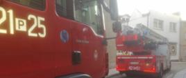Na zdjęciu widać dwa samochody pożarnicze zadysponowane do pożaru mieszkania, które stoją na drodze jednokierunkowej