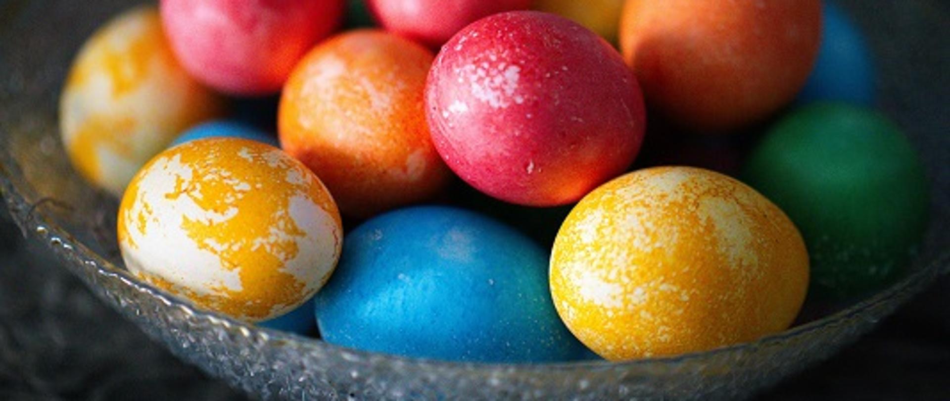 na stole stoi talerz, a na nim leżą kolorowe pisanki 