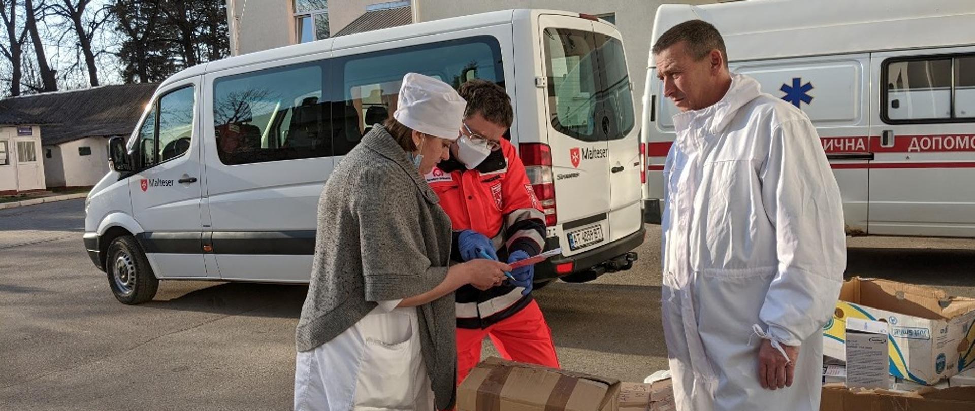 Trzy osoby przed minivanem i między paczkami podpisują dokumenty