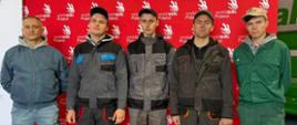 Na tle czeronej tablicy z logo World Skills Poland stoi pięciu mężczyzn, pozują patrząc w aparat