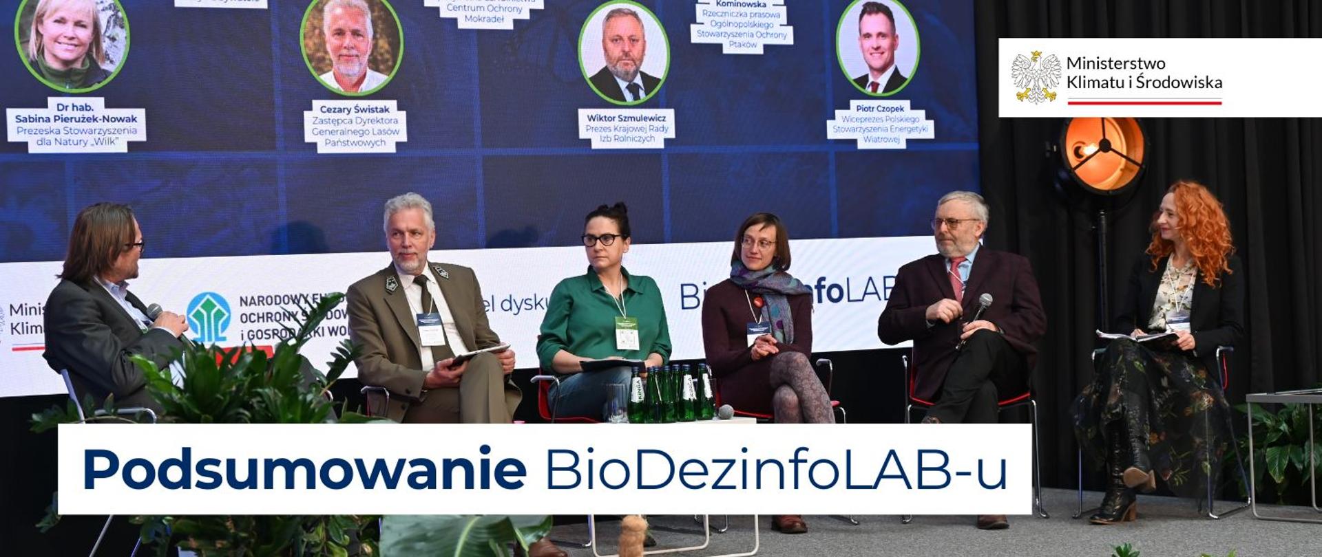 Na zdjęciu widać 6 osób siedzących na scenie z mikrofonami. Za nimi znajduje się duży ekran, na którym widnieją zdjęcia prelegentów wraz z podpisami.