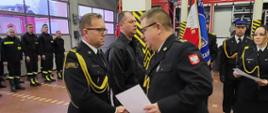 Opis: Zastępca Pomorskiego Komendanta Wojewódzkiego PSP bryg. Wojciech Berent wręcza akty mianowania na wyższe stanowisko służbowe funkcjonariuszom. W tle poczet sztandarowy, Strażacy w dwuszeregi i nowy samochód ratowniczo – gaśniczy.