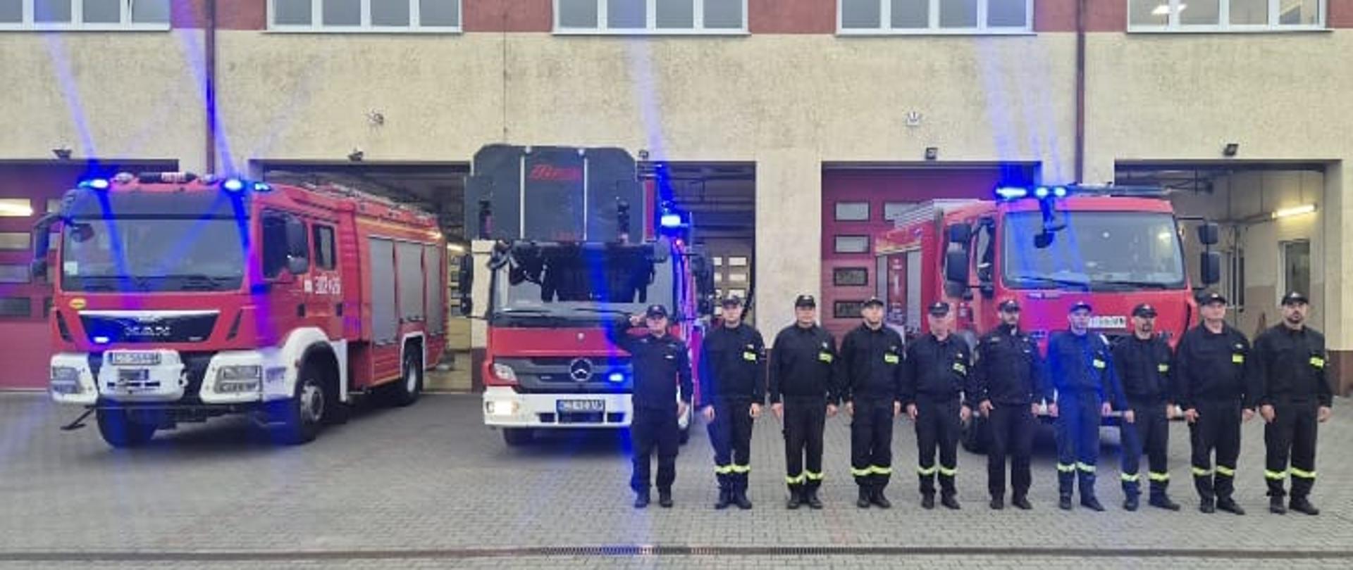 Zbiórka przy JRG2. Strażacy w szeregu za nimi samochody pożarnicze. 