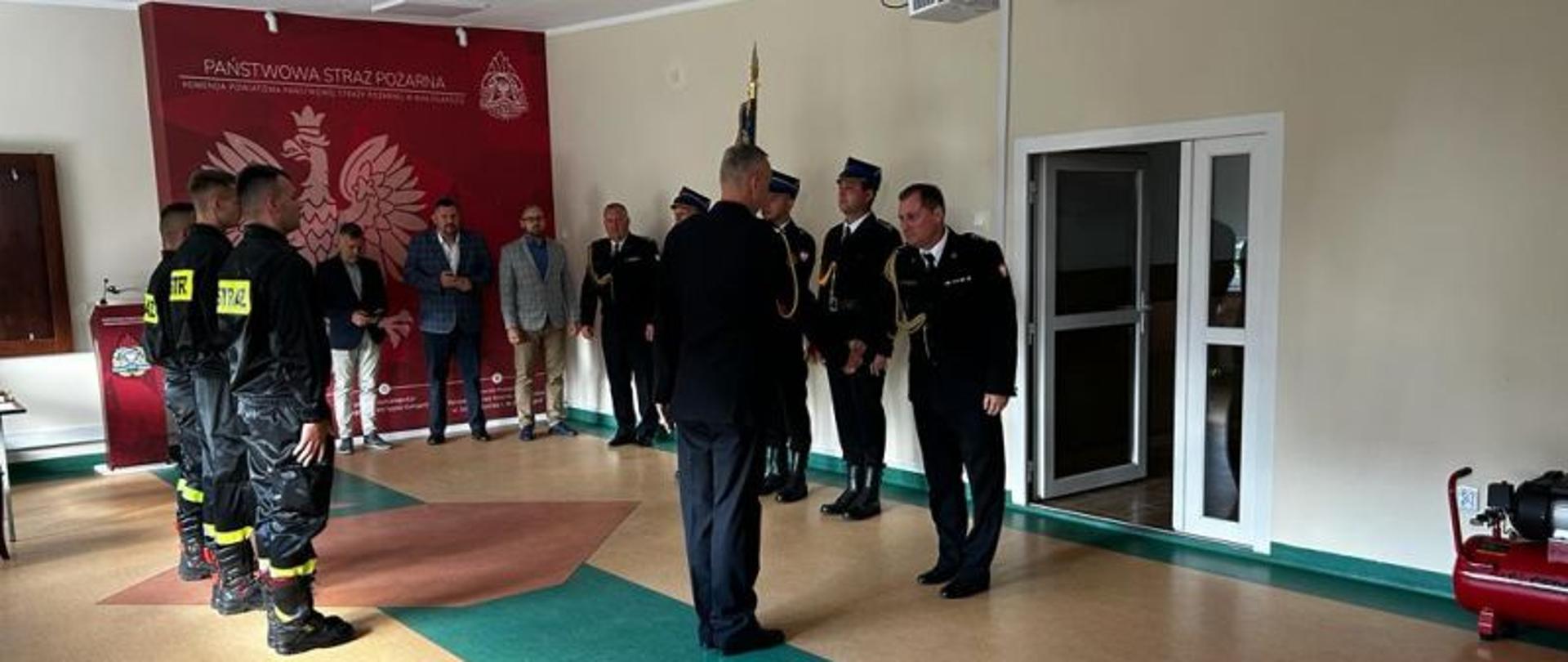 Zdjęcie wykonane na świetlicy komendy. Przedstawia moment meldunku prowadzącego uroczystości strażaka dla Komendanta PSP.