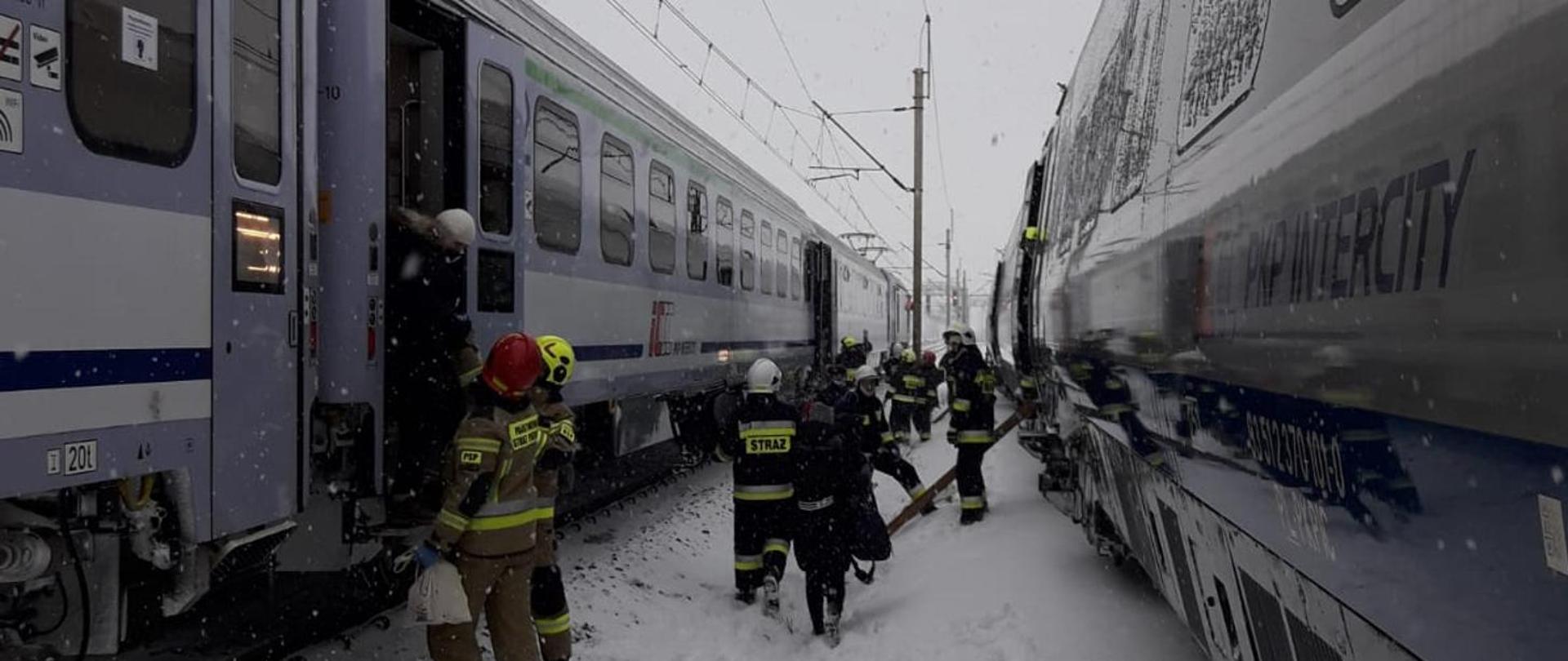 Na zdjęciu widać dwa pociągi, między nimi strażacy przeprowadzają pasażerów z jednego do drugiego
