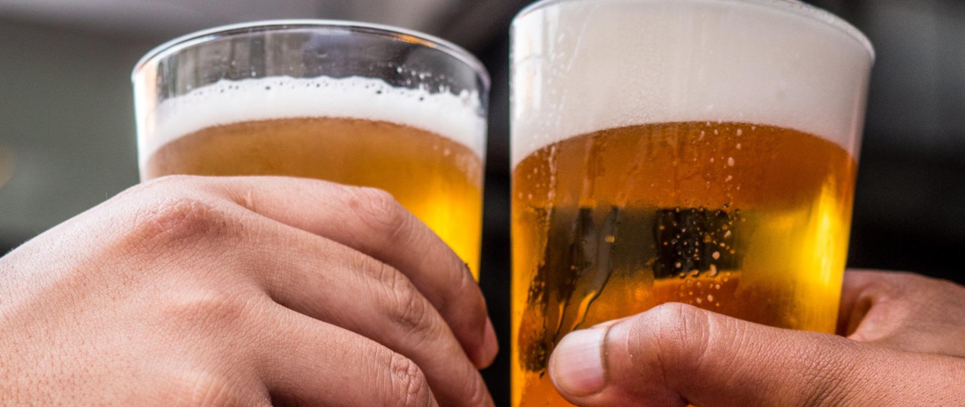 Fotografia przedstawiająca dłonie dwóch osób trzymające szklanki z napojem gazowanym z pianką