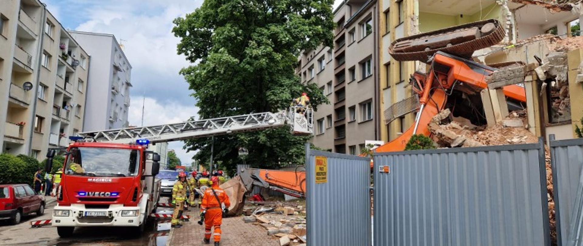 Zdjęcie przedstawia ulicę J i J Śniadeckich. Po lewej stronie zaparkowała drabina mechaniczna. Po prawej widać wyburzany budynek biurowy a znad aluminiowego ogrodzenia wystaje część jezdna przewróconej koparki. Fragment z łyżką ładunkowa leży na chodniku. 