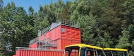 sześciu strażaków ubranych w ubrania specjalne pracuje przy raku autobusu, w tle czerwone kontenery