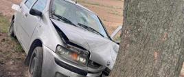 Zdjęcie przedstawia zniszczony samochód osobowy po uderzeniu w drzewo. 