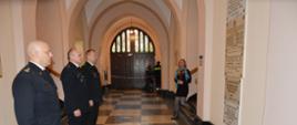 Zdjęcie przedstawia trzech komendantów miejskich PSP w Krakowie oddających honor przed tablicami pamięci w holu Komendy Miejskiej PSP w Krakowie.