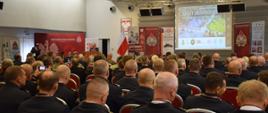 Pełna sala słuchaczy wykładów jednego z prelegentów. Na pierwszym planie widoczni strażacy PSP w umundurowaniu wyjściowym.