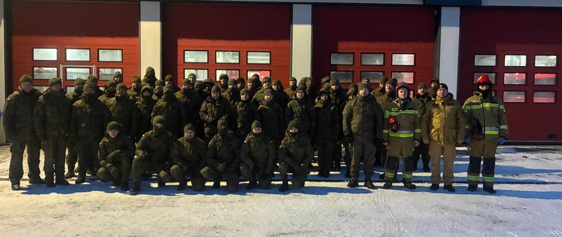 Na zdjęciu widoczni żołenierze Wojsk Obrony Terytorialnej oraz funkcjonariusze PSP . Zdjęcie grupowe na tle bram garażowym jednostki PSP.