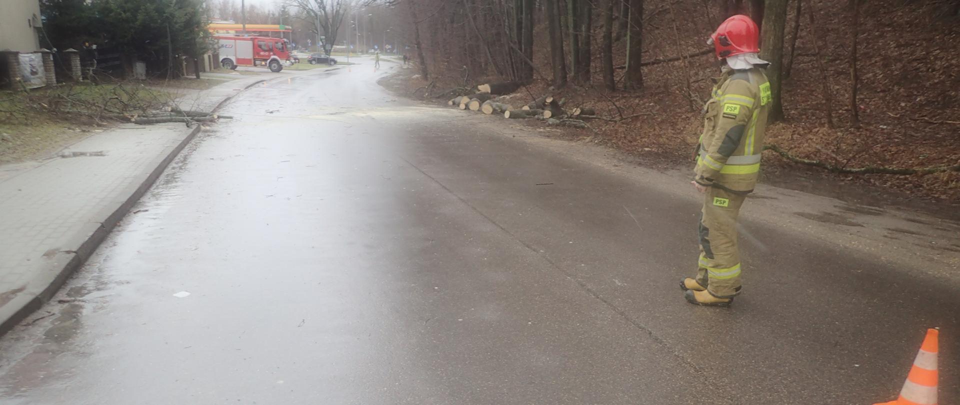 Zdjęcie przedstawia strażaka zabezpieczającego miejsce zdarzenia po uszkodzeniu linii energetycznej przez wiatrołom 