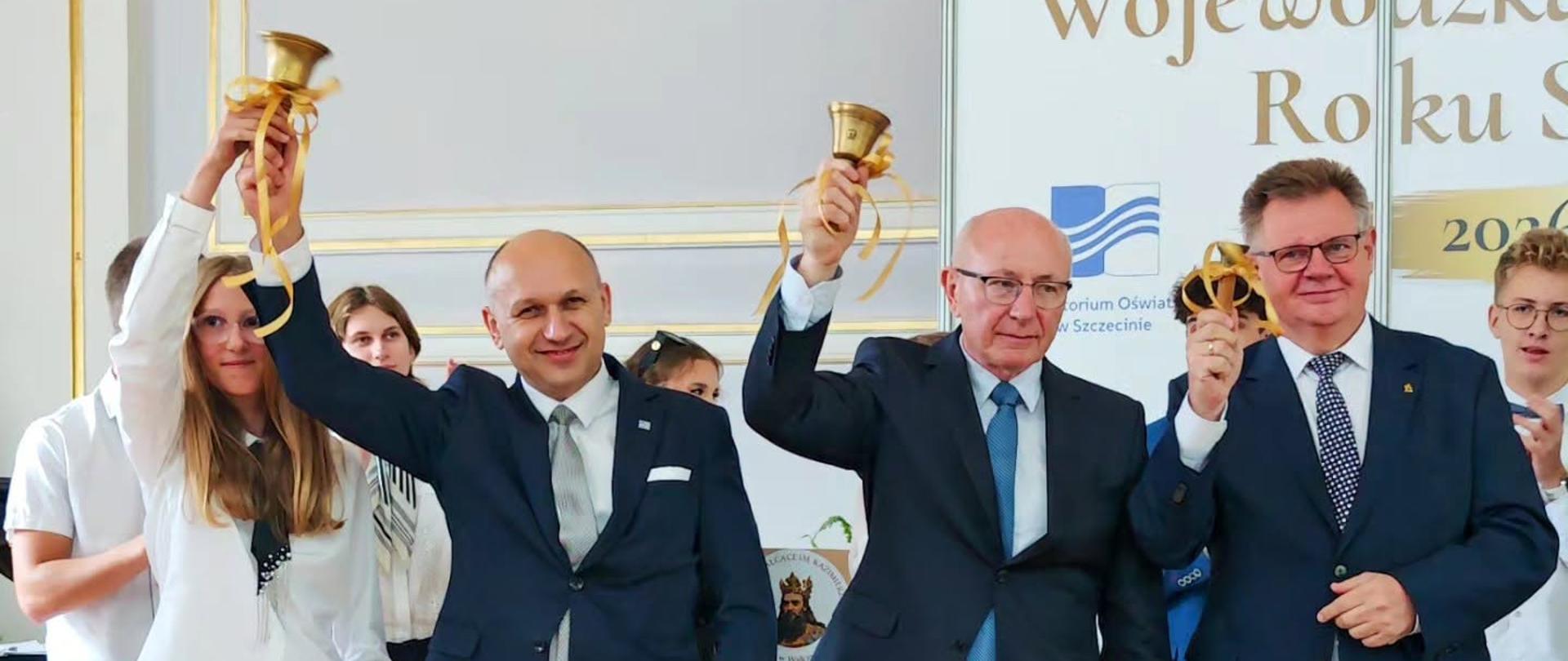 Cztery osoby trzymające dzwonki nad głowami, w tle napis wojewódzka inauguracja roku 