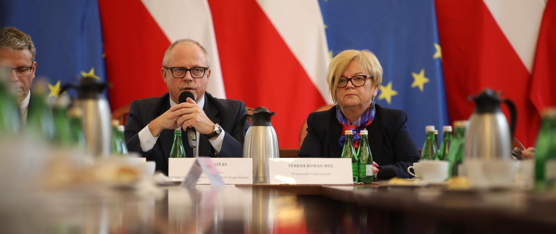 Wiceminister Jacek Protas z mikrofonem w ręku przy stole. Obok wojewoda podkarpacka.