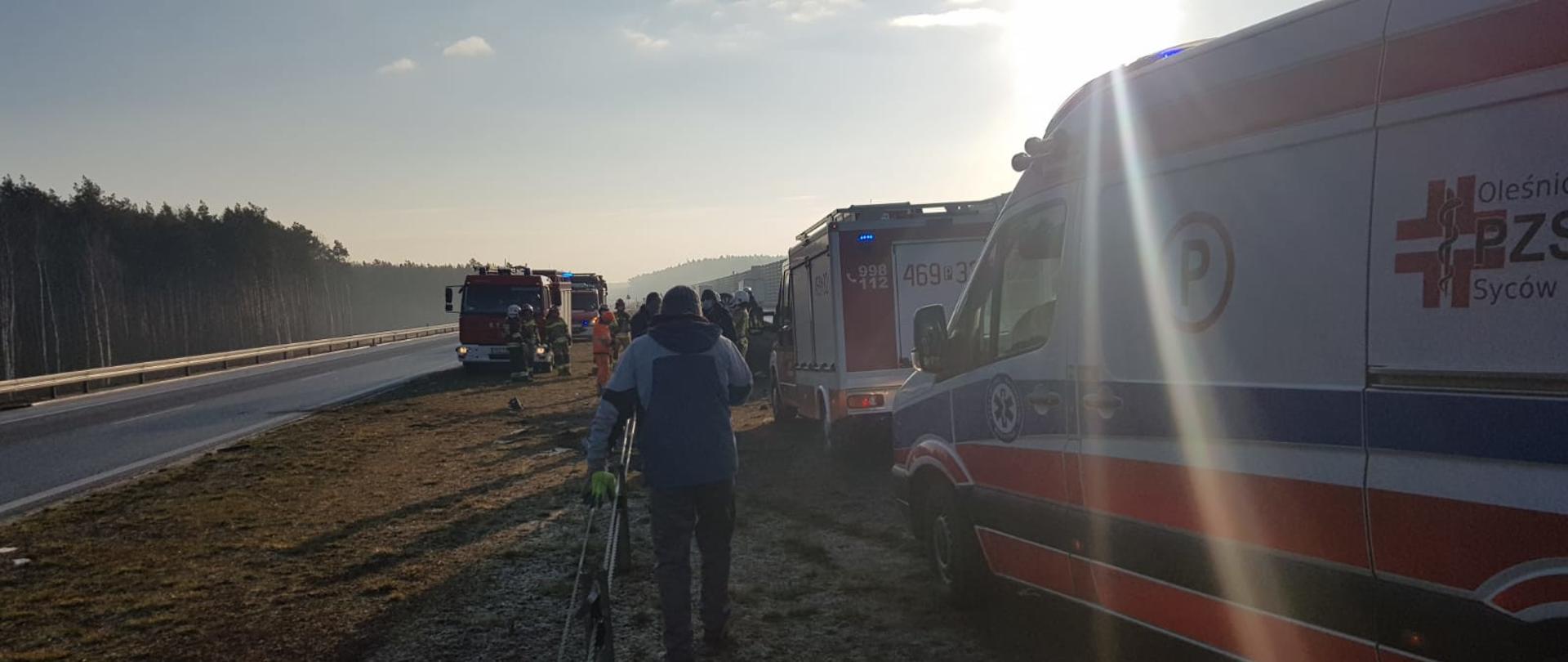 Teren działań służb. Widoczne zastępy strażaków oraz zespół pogotowia ratunkowego.