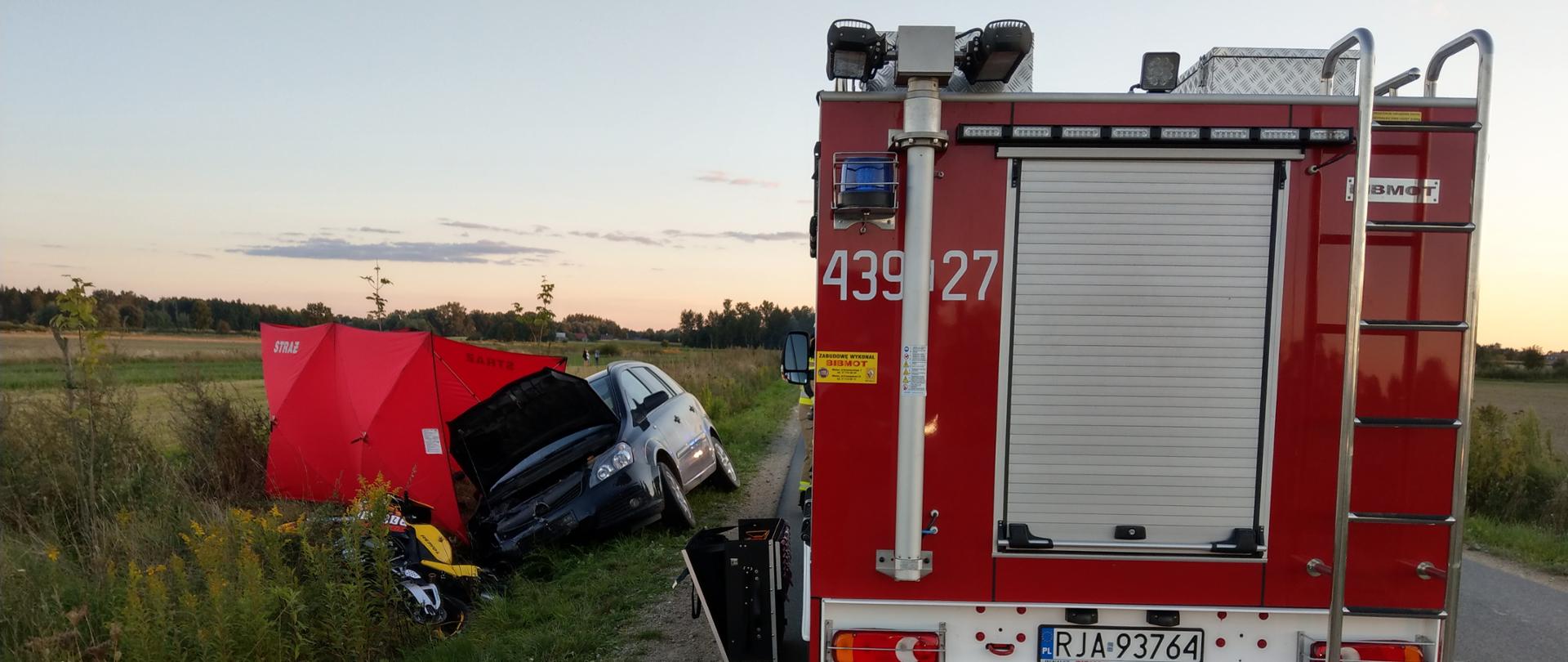 Na zdjęciu widzimy tył lekkiego samochodu ratownictwa technicznego, należącego do OSP Laszki. Za nim, po lewej widać leżący w rowie motocykl Honda CBR, samochód osobowy Opel Zafira, a także parawan strażacki