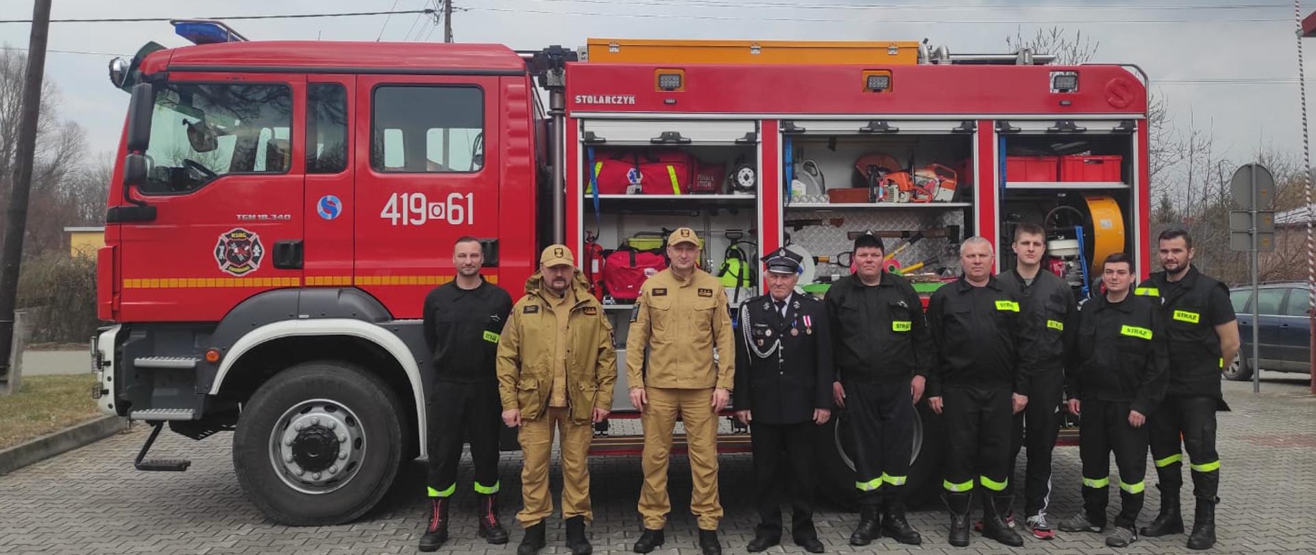 Na zdjęciu widoczny Zastępca Opolskiego Komendanta Wojewódzkiego PSP, Komendant Powiatowy PSP w Głubczycach w mundurach służbowych oraz strażacy Ochotniczej Straży Pożarnej w Grobnikach w mundurach koszarowych, na tle samochodu ratowniczo gaśniczego z jednostki OSP Grobniki.