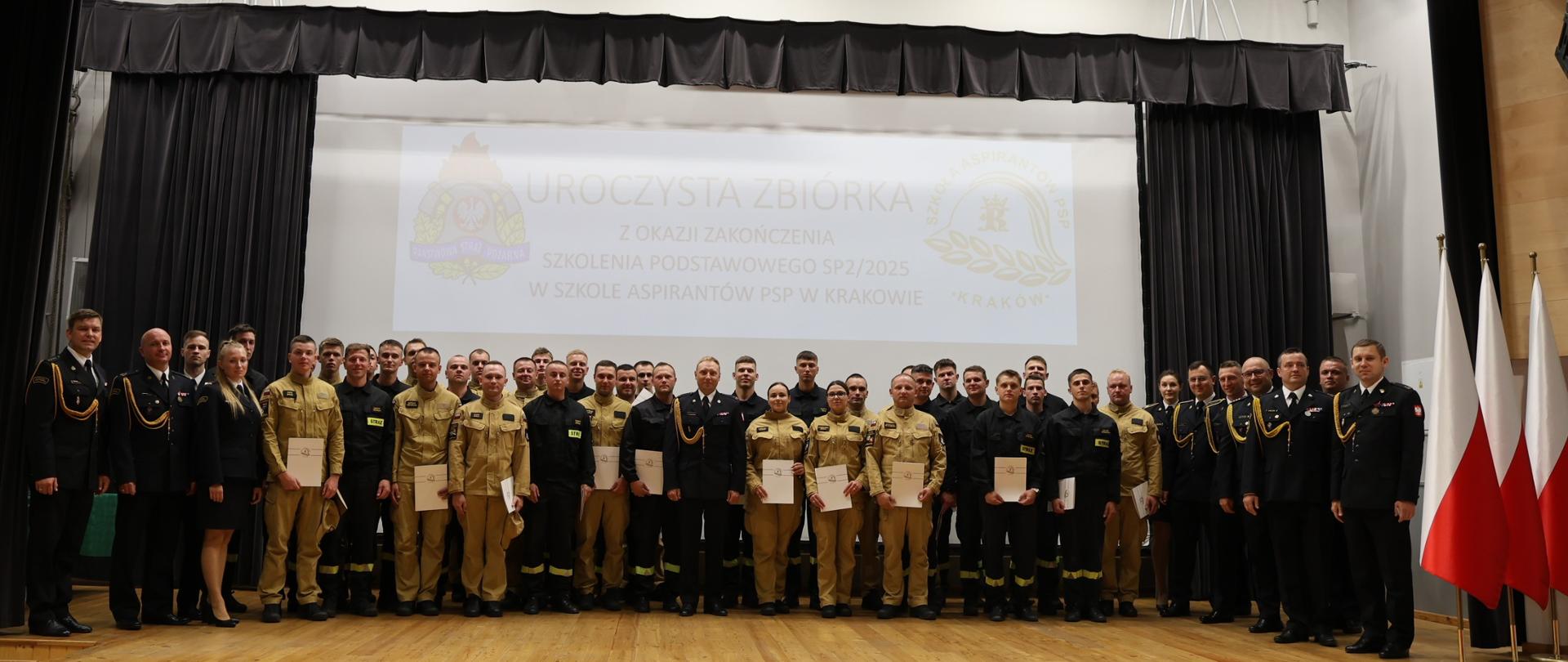 Pamiątkowe zdjęcie absolwentów szkolenia. Na scenie stoją trzymający w rękach teczki z dokumentami uczestnicy wraz z Zastępcą Komendanta Szkoły i pracownikami. 