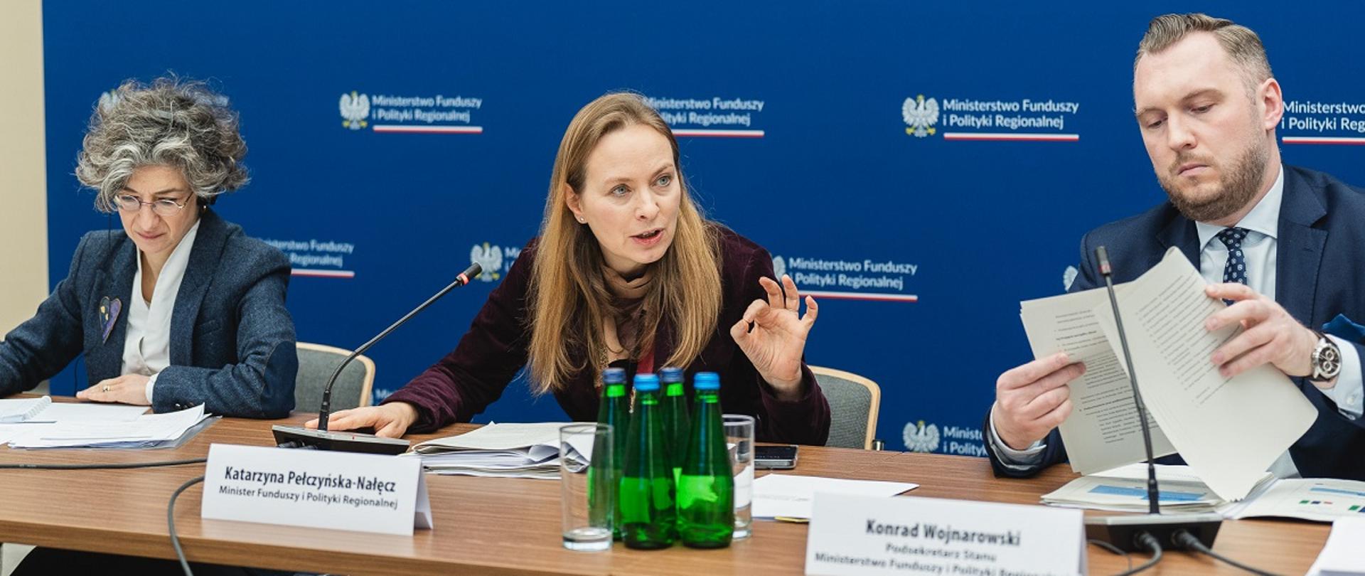 Posiedzenie Komitetu ds. Umowy Partnerstwa na lata 2021-2027, minister funduszy i polityki regionalnej Katarzyna Pełczyńska-Nałęcz siedzi przy stole, po jej lewej stronie siedzi Dyrektorka ds. Wdrażania w Dyrekcji Generalnej ds. Polityki Regionalnej i Miejskiej (DG REGIO) Emma Toledano-Laredo, zaś po prawej stronie wiceminister funduszy i polityki regionalnej Konrad Wojnarowski