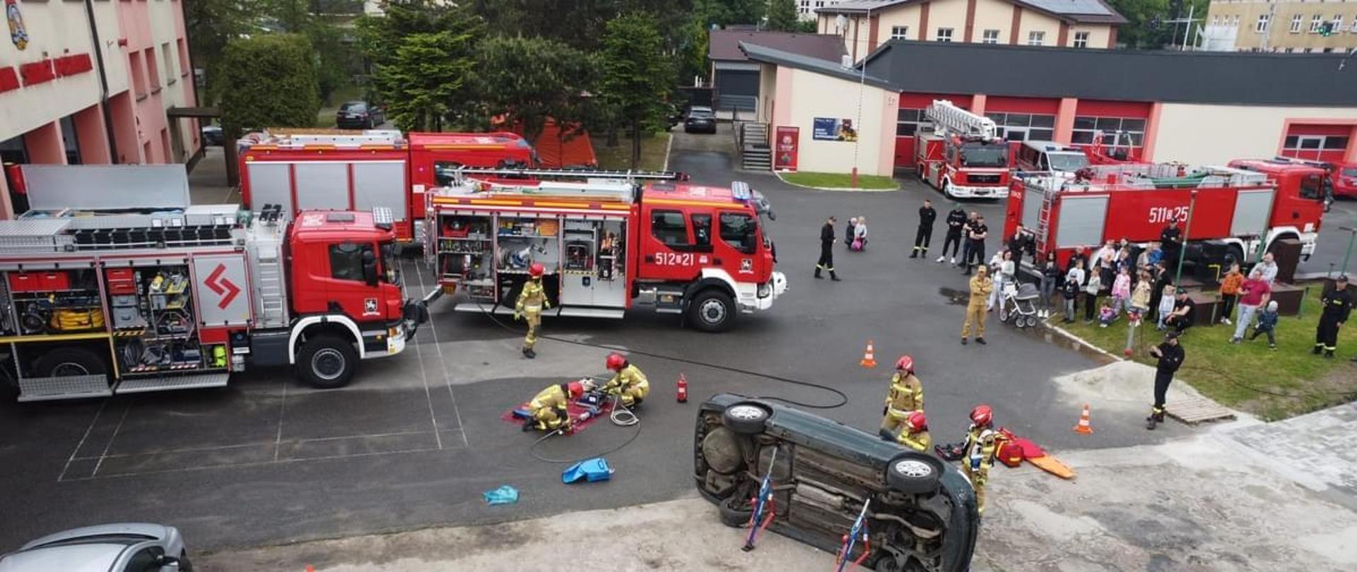 Na zdjęciu znajdują się pojazdy pożarnicze oraz strażacy i mieszkańcy.