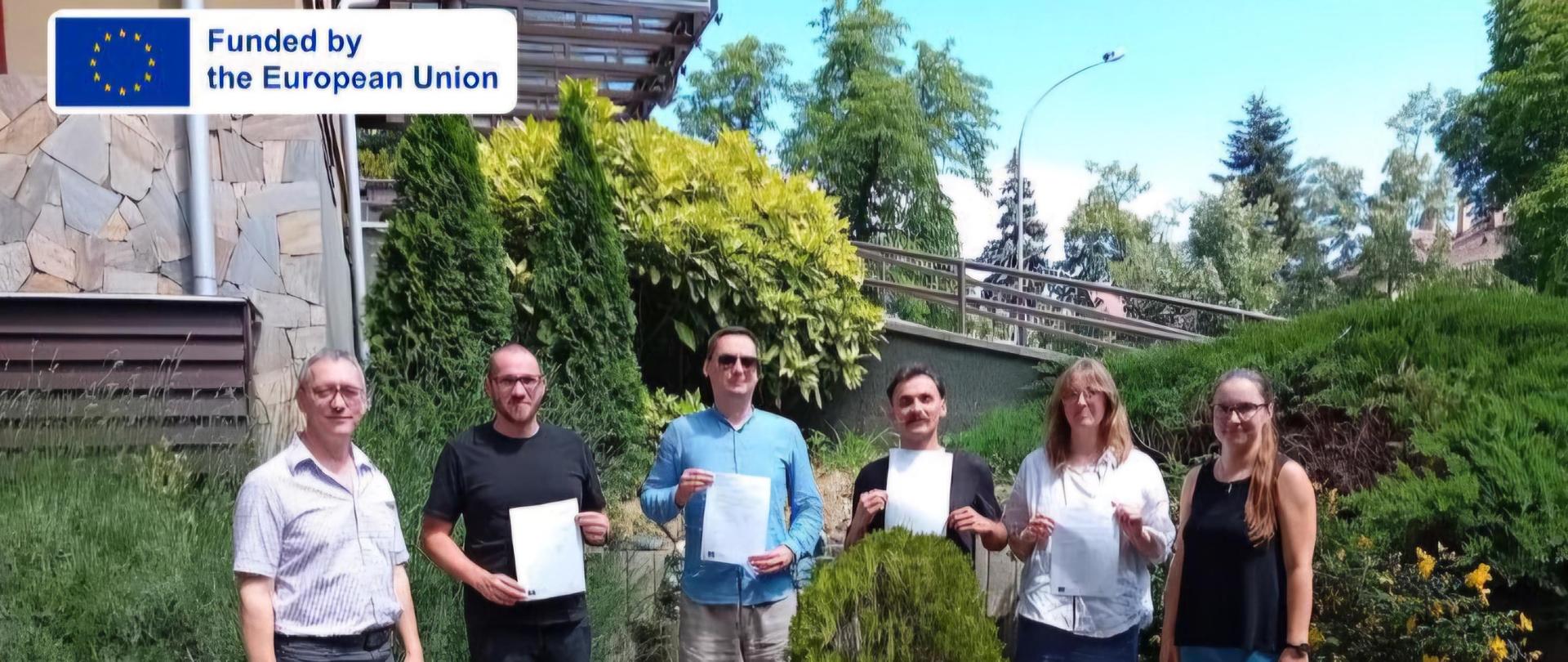 Zdjęcie nauczycieli z certyfikatami uczestnictwa na tle roślin. Zdjęcie dostaliśmy od Reményi Ede Zenei Alapfokú Művészeti iskola