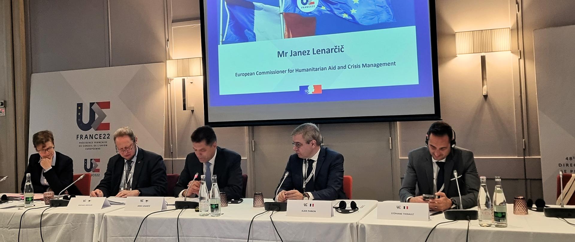 Pięciu mężczyzn siedzących przy stole konferencyjnym za nimi widoczny jest ekran projektora z wyświetlaną prezentacją. 