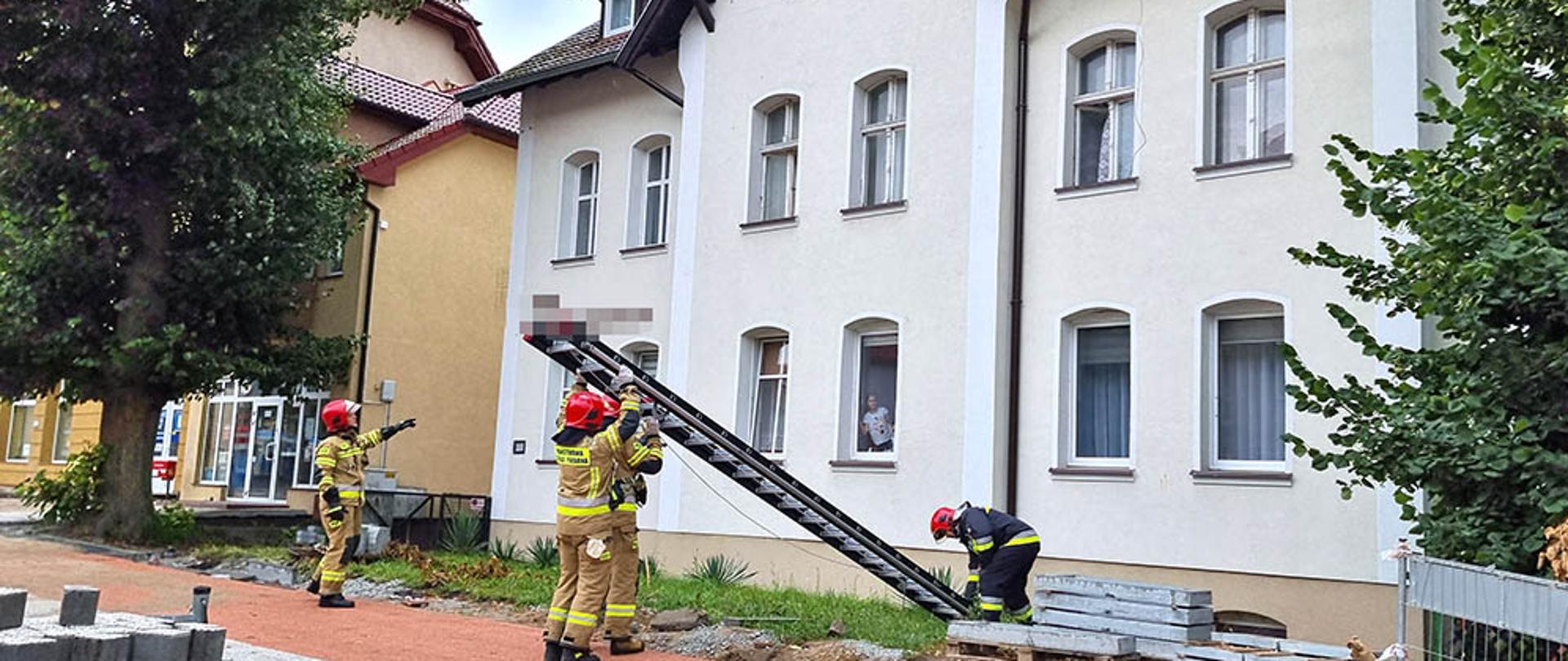 Zdjęcie przedstawia strażaków ustawiających drabinę do okna by dostać się do mieszkania
