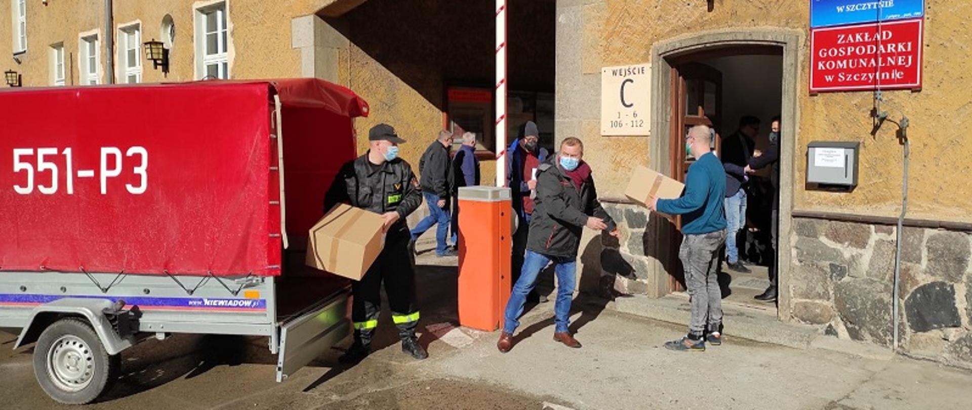Zdjęcie przedstawia funkcjonariusza, którym przekazuje kartony z maseczkami ochronnymi dla pracowników urzędu miasta