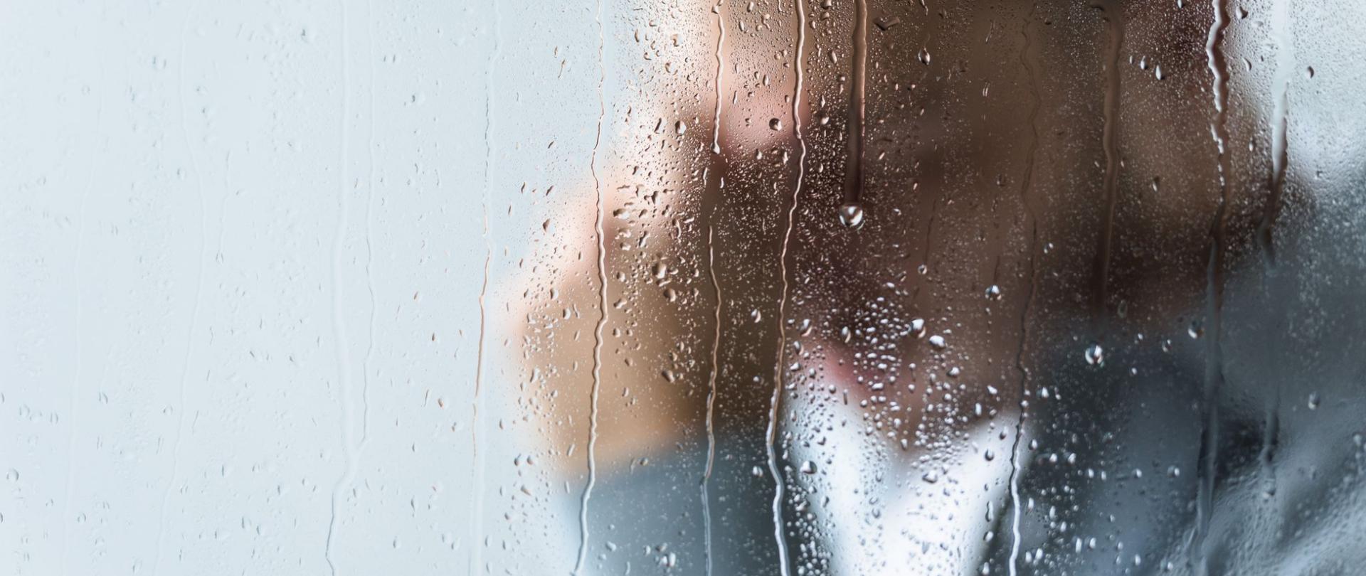 Na zdjęciu jest popiersie mężczyzny stojącego za szybą na której widoczne są krople wody.
