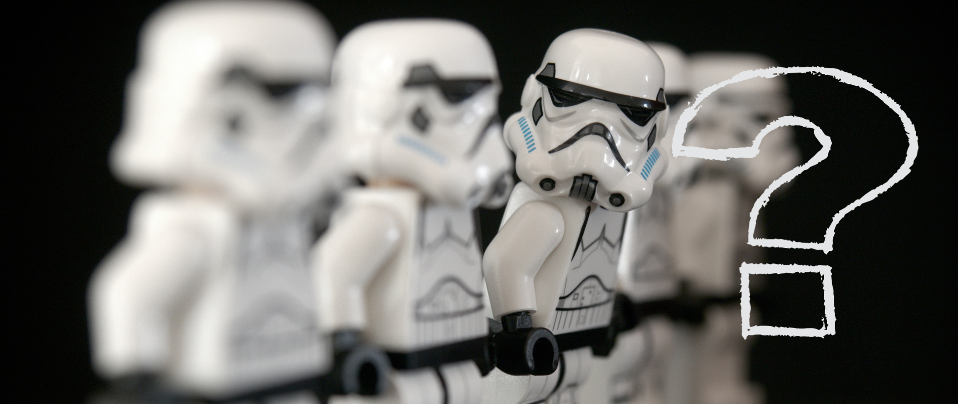 Cztery ludziki lego stojące w szeregu. Na nich graficzny znak zapytania