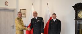 Pomorski komendant wojewódzki Państwowej Straży Pożarnej trzyma medal, druh ochotniczej straży pożarnej gratuluje wyróżnienia w obecności komendanta powiatowego Państwowej Straży Pożarnej w Pucku. 