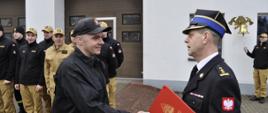 Zdjęcie przedstawia mł. ogn. Daniela Brzóskę odbierającego nagrodę jubileuszową z rąk Komendanta Powiatowego PSP w Brodnicy st. bryg. Andrzeja Góreckiego. W tle strażacy podziału bojowego JRG w Brodnicy.