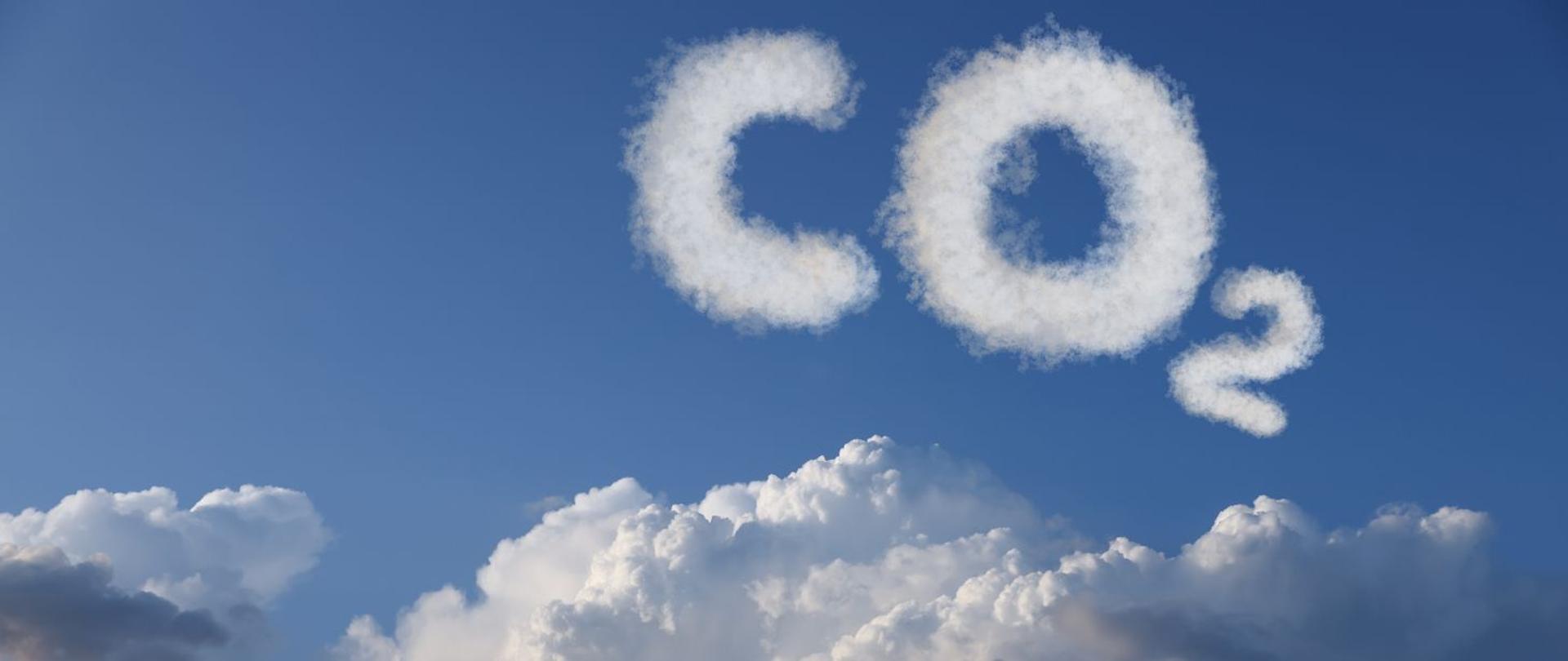 na zdjęciu widnieje napis CO2, który unosi się na błękitnym niebie z białymi chmurami. 