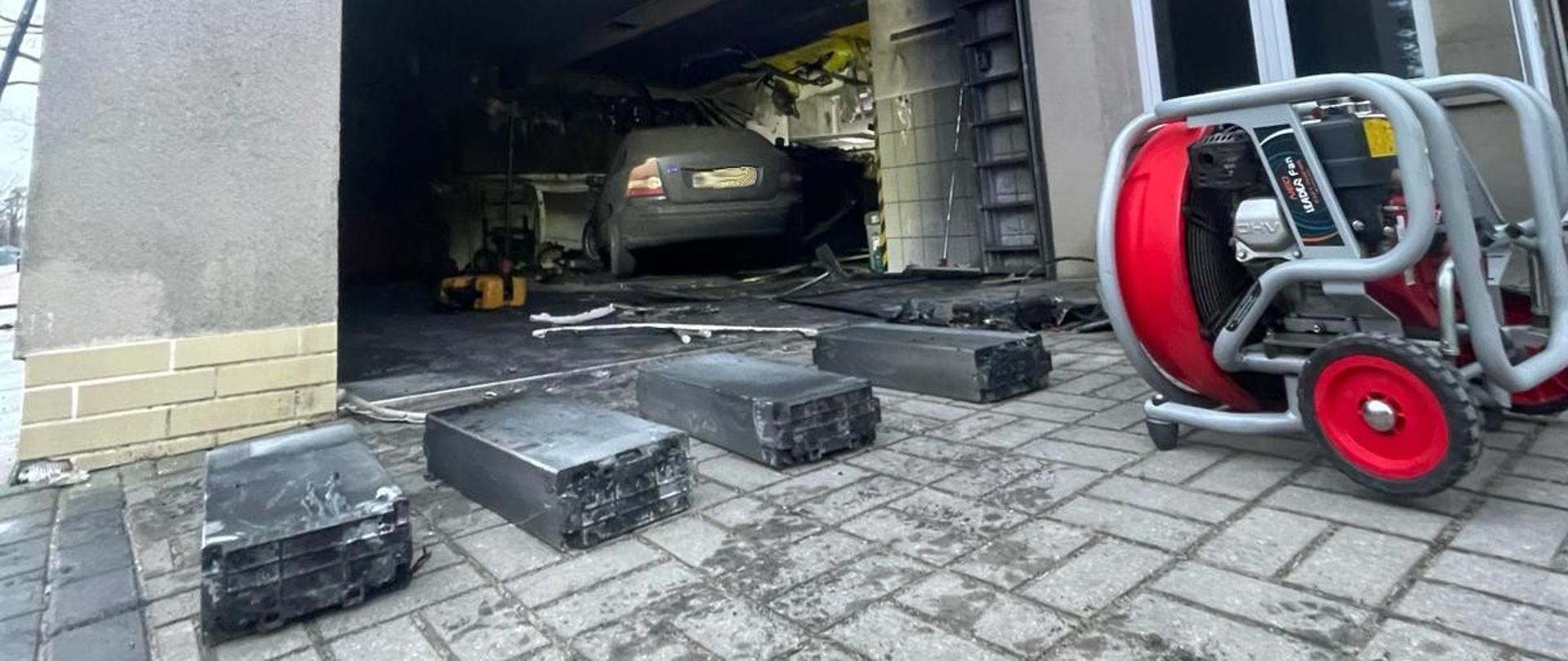 Zdjęcie przedstawia wyniesione z pożaru baterie elektryczne i wentylator do oddymiania pomieszczenia.