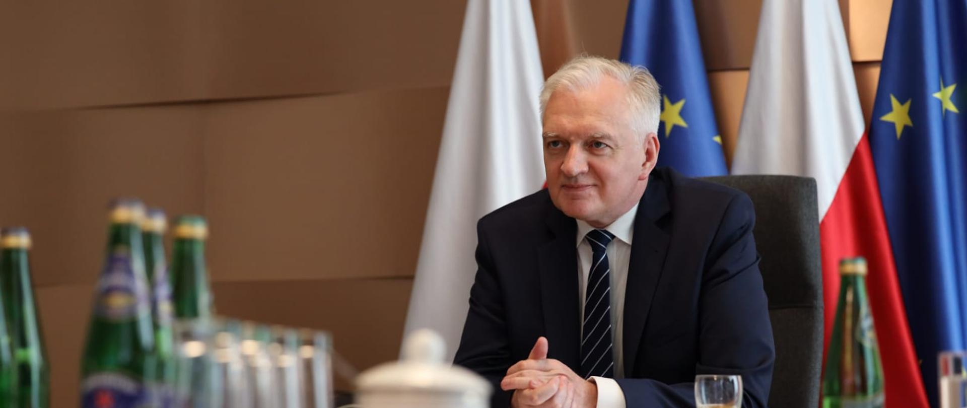 Deputy Prime Minister Jarosław Gowid during the videoconference. He sits at the table. Polish and European Union Flags in the background.