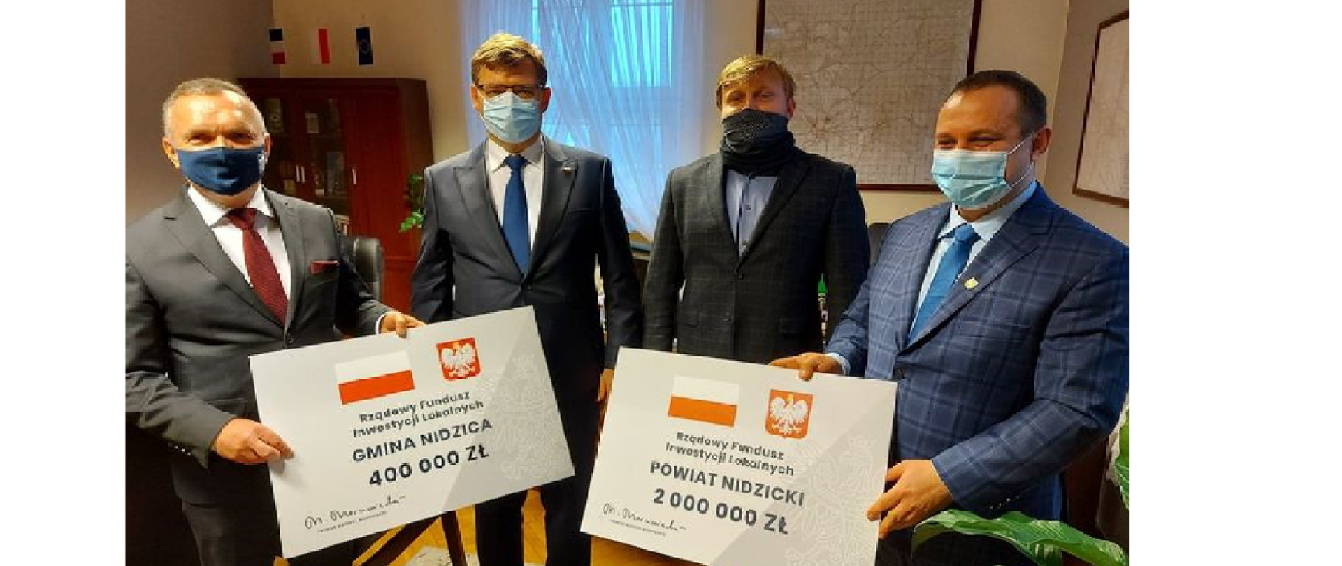 Wojewoda stoi i jeszcze 3 ludzi,a dwóch trzyma duże symboliczne czeki z kwotami