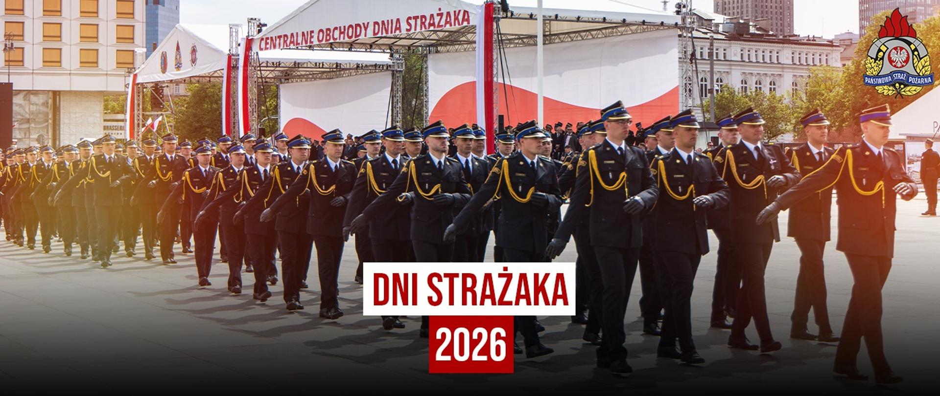 Grafika promująca Dni Strażaka 2026. W tle kolumna strażaków Państwowej Straży Pożarnej w mundurach galowych maszeruje podczas Centralnych Obchodów Dnia Strażaka. Na środku znajduje się napis „Dni Strażaka 2026”, a w prawym górnym rogu widoczne jest logo Państwowej Straży Pożarnej.