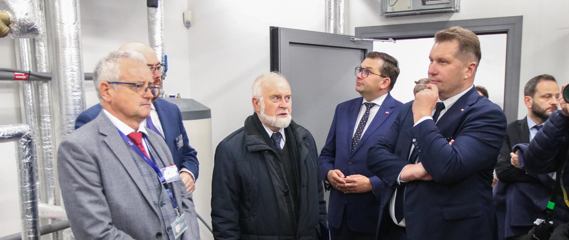 Grupa mężczyzn w garniturach. Wśród nich mionister Czarnek podpiera ręką brodę