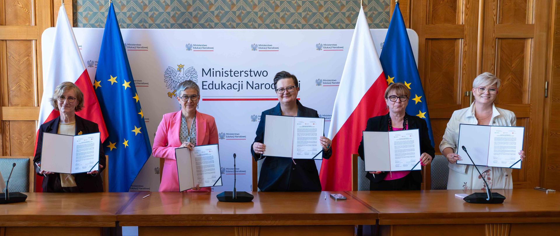 Na zdjęciu wiceminister Katarzyna Lubnauer wraz z wiceminister Ministerstwa Nauki i Szkolnictwa Wyższego Maria Mrówczyńska oraz przedstawicielami miast: Krakowa, WArszawy i Rzeszowa. Kobiety stoją przy stole i trzymają podpisane deklaracje współpracy.

