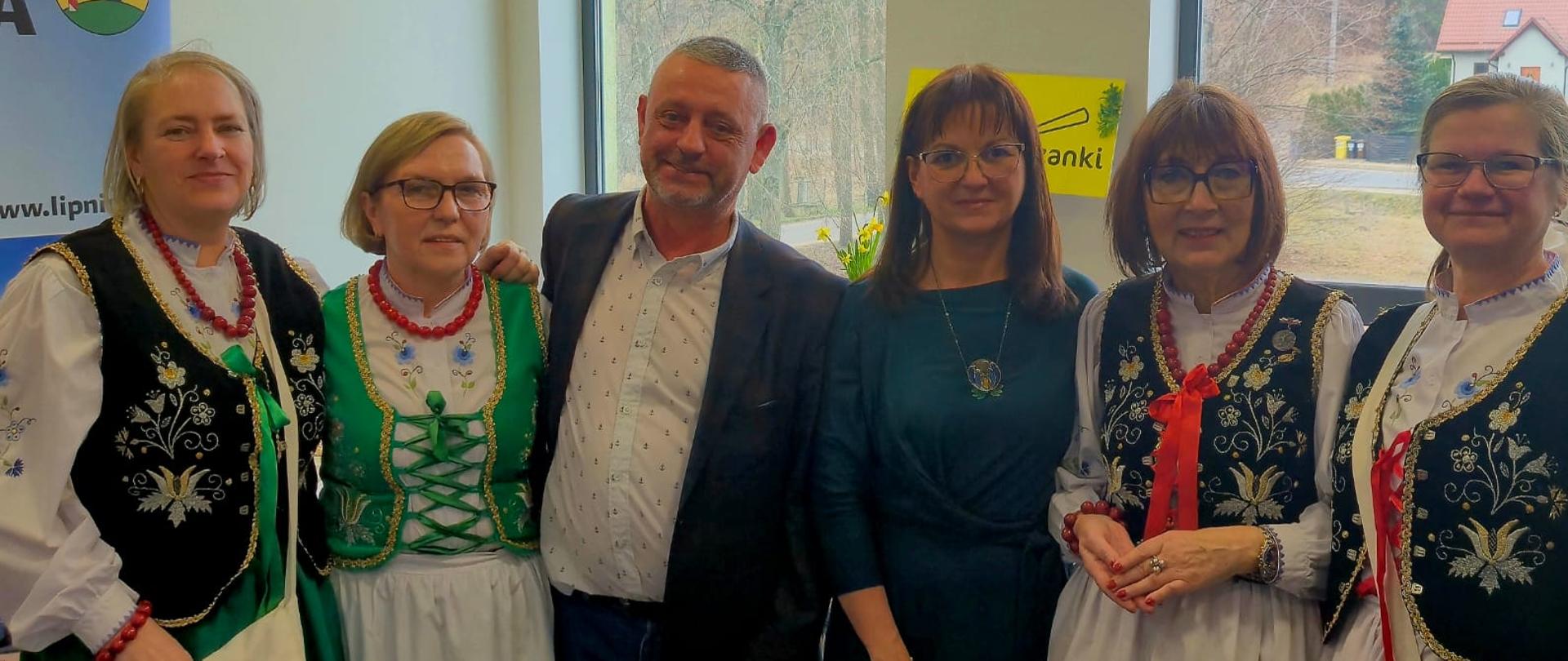 Mężczyzna stojący pośród pięciu kobiet w strojach ludowych 