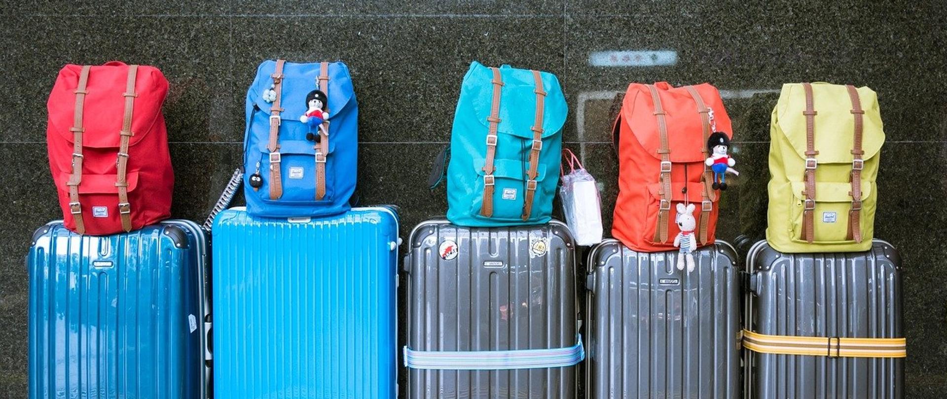 pod ścianą na dworcu stoi 5 walizek, a na walizkach 5 plecaków podróżnych 