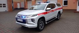 Zdjęcie przedstawia nowy samochód strażacki osobowy specjalny Mitsubishi L200.
W tle budynek Komendy.
