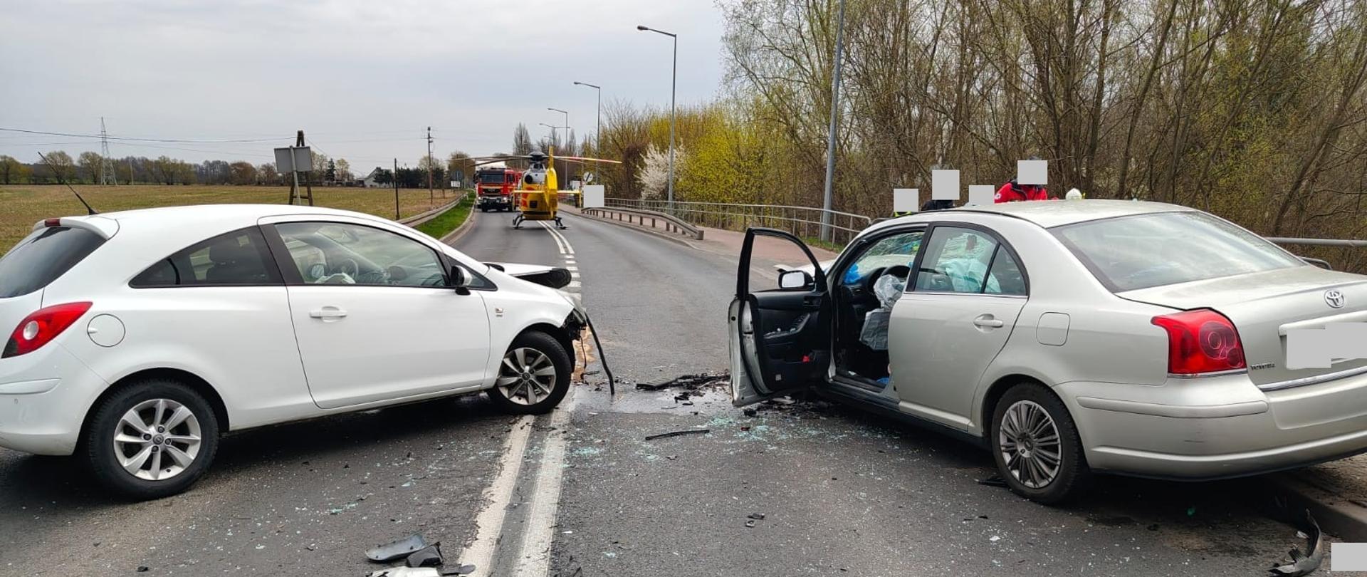 Dwa uszkodzone pojazdy i śmigłowiec na drodze