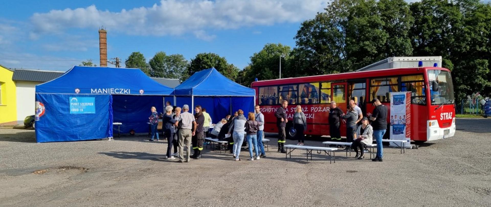 Na zdjęciu autobus OSP, ludzie przy ławkach oraz namioty przeznaczone na punkty szczepień