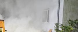 Pożar w budynku mieszkalnym jednorodzinnym. Przed budynkiem widać silne zadymienie