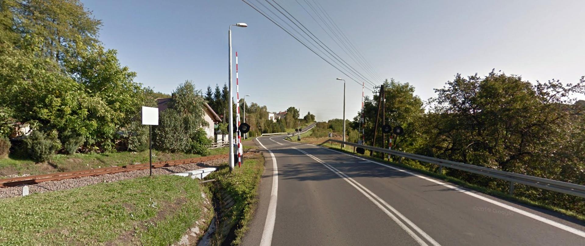 Droga i przejazd kolejowy, szlaban jest otwarty świeci słońce, na drodze nie ma samochodów